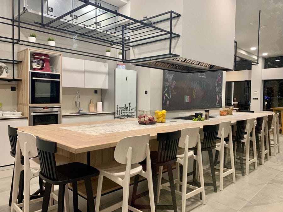 Modern kitchen with a large wooden table, black and white chairs, and sleek appliances, including a stylish fridge that completes the contemporary aesthetic.